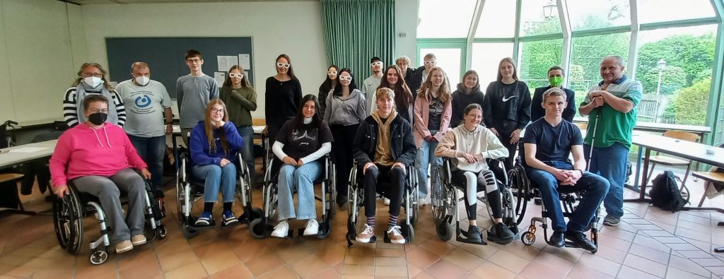 Gruppenfoto FOS Klasse 11Sa mit Mitgliedern des Behindertenbeirats Ansbach. Eine Schüler*innen sitzen in Rollstühlen, einige tragen Sehbehinderungssimulationsbrillen.